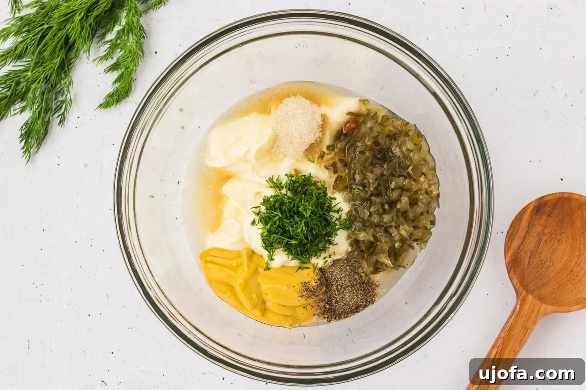 A glass bowl filled with gluten-free potato salad dressing ingredients, including mayonnaise, mustard, dill, relish, and seasonings.
