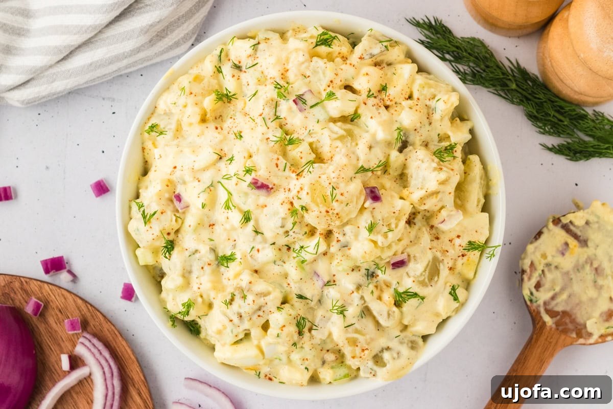 A freshly prepared gluten-free potato salad in a white bowl, garnished with fresh dill and a dusting of paprika.