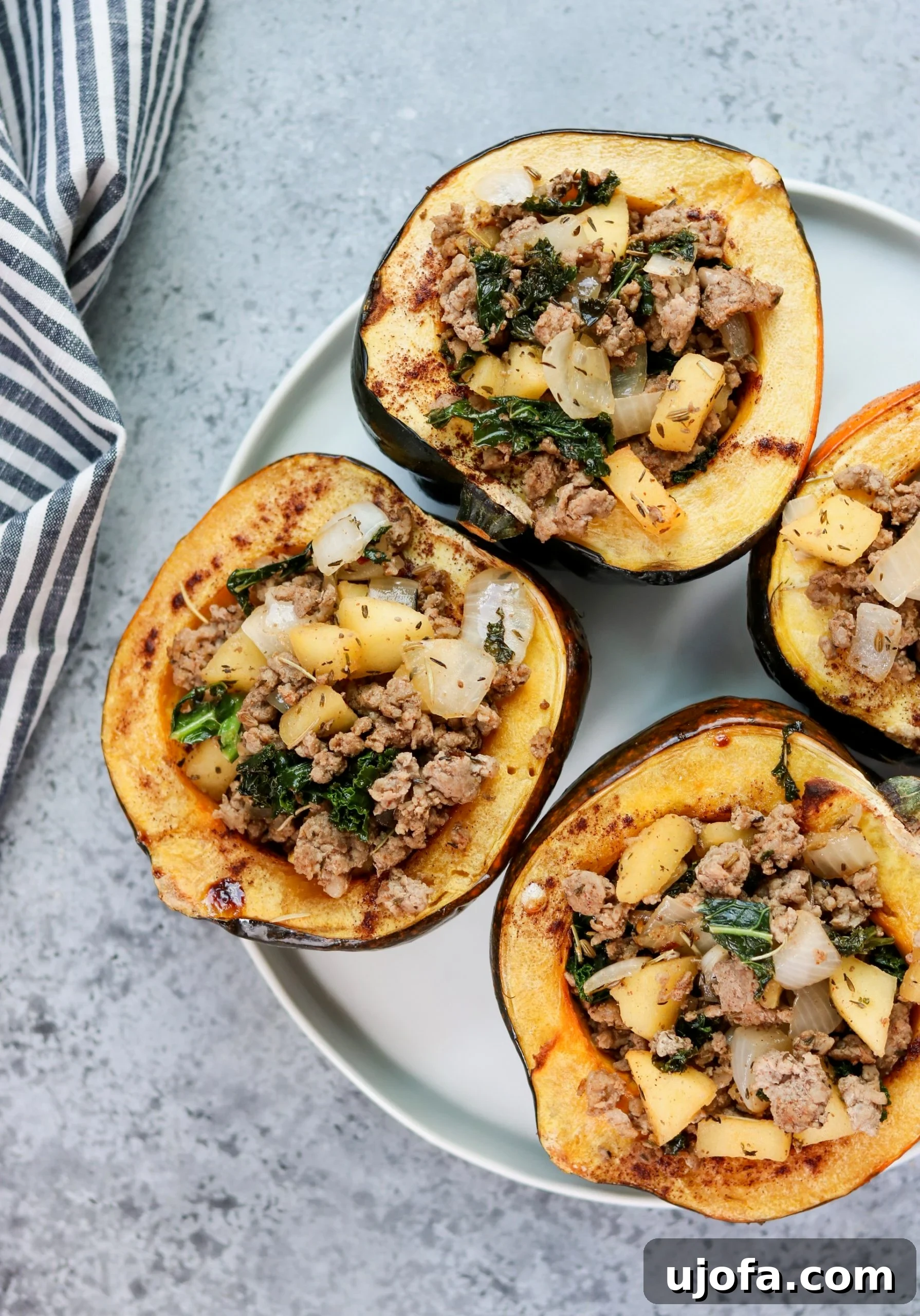 Muhteşem Paleo Şükran Günü Sofrası İçin Her Şey 8 Two halves of roasted acorn squash, beautifully stuffed with a savory mixture of sausage, herbs, and other festive ingredients, presented on a plate, highlighting their rustic charm.