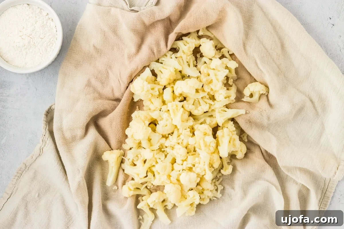 Cooked and drained cauliflower florets gathered inside a clean kitchen towel, carefully twisted and squeezed by hands to remove every last drop of excess moisture. This critical step prepares the cauliflower for making perfectly textured gnocchi dough.