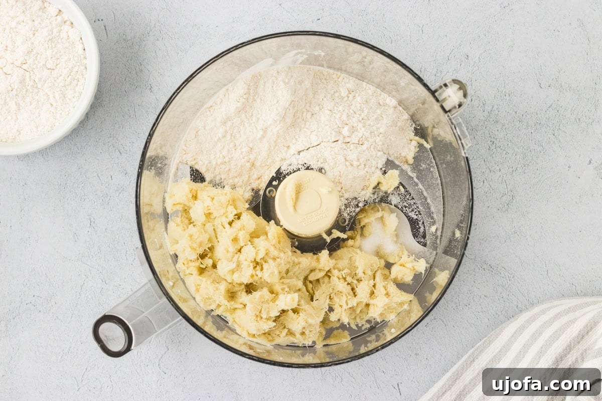 A top-down view inside a food processor bowl, showcasing a finely blended and cohesive mixture of mashed cauliflower, gluten-free flour, and salt. The ingredients have come together to form a soft, slightly sticky dough, ideal for cauliflower gnocchi. A small bowl of extra flour is conveniently placed nearby, ready for any necessary adjustments.