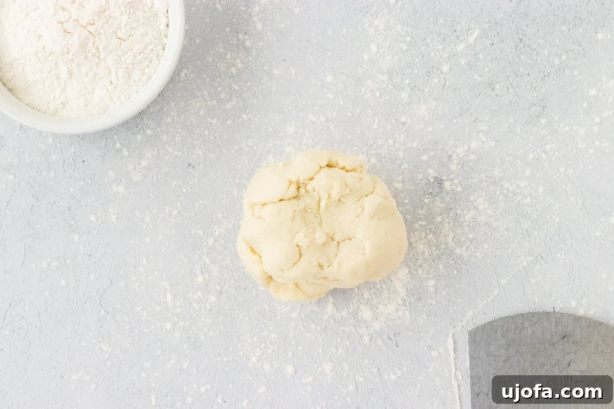 A perfectly formed, smooth, and round ball of cauliflower gnocchi dough resting on a lightly floured wooden surface. The dough appears uniform in texture and ready for the next crucial stage of being divided and shaped into individual gnocchi pieces.