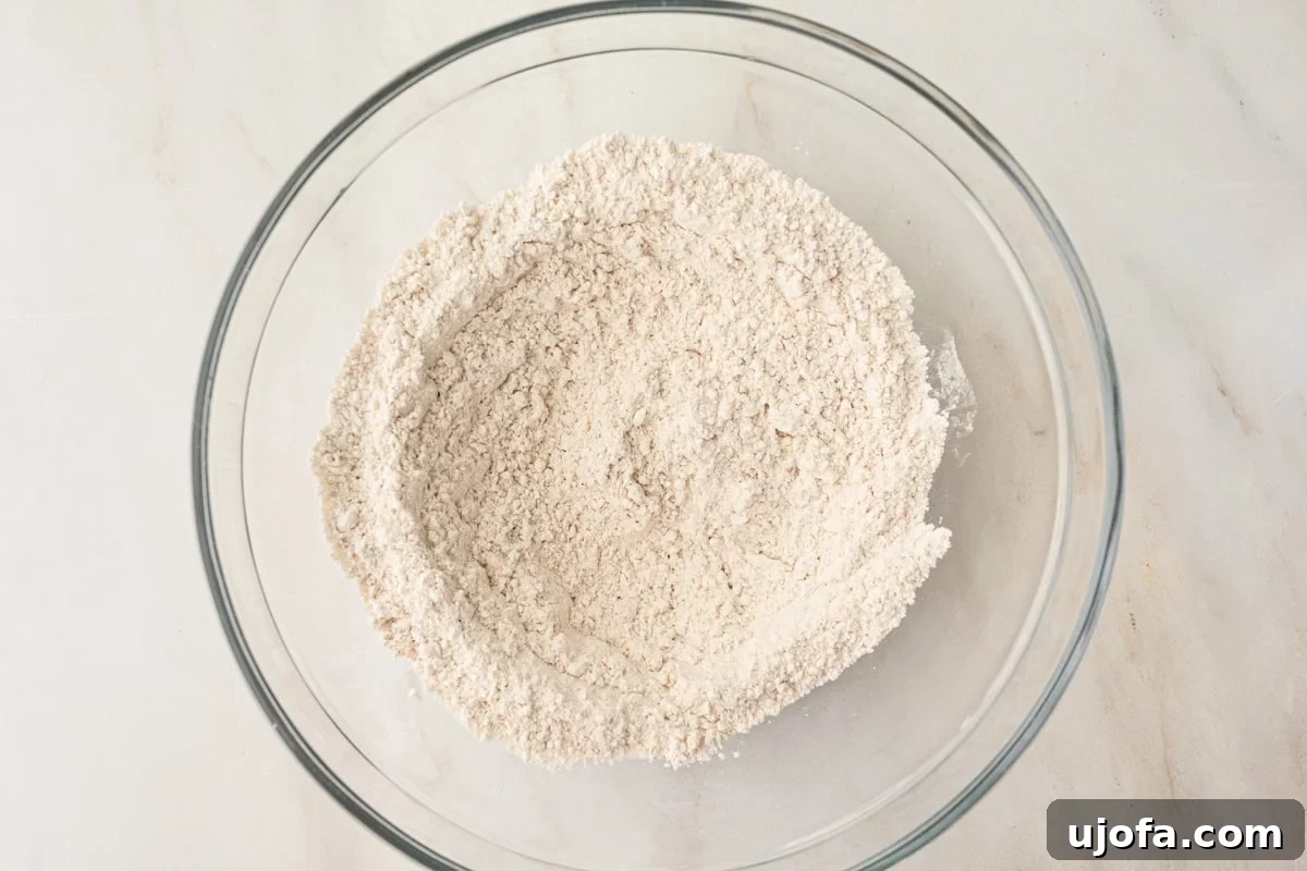 A glass mixing bowl with whisked dry ingredients, including gluten-free flour and spices, creating a light, airy mixture before combining with wet ingredients.
