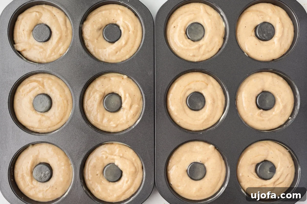 Donut batter piped into a greased donut pan, showing the smooth, thick consistency of the gluten-free mixture before baking.