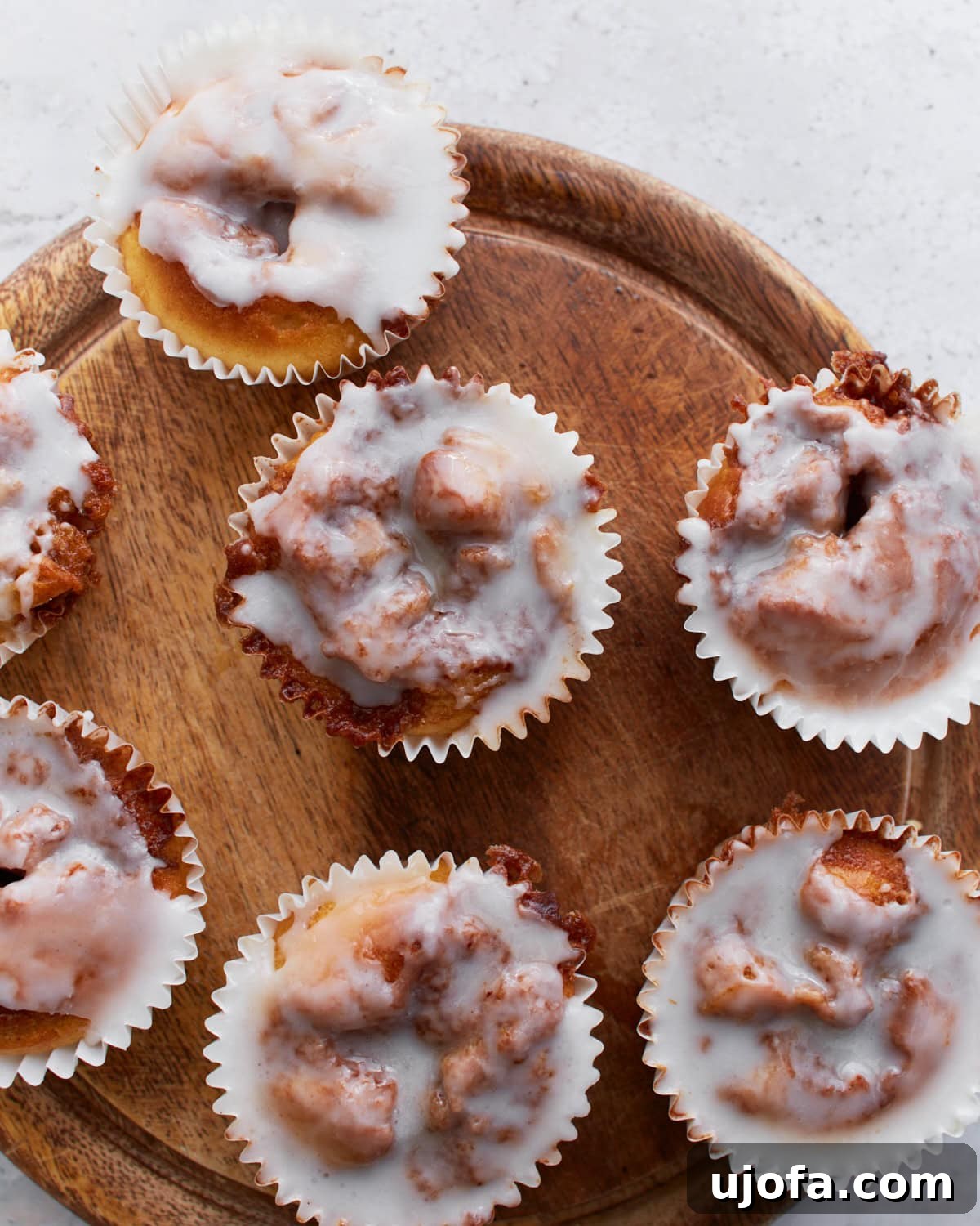 Gluten-Free Cinnamon Swirl Delights 2 Overhead view of glazed gluten-free cinnamon roll muffins arranged on a round wooden board, showing their gooey swirls and shiny icing.