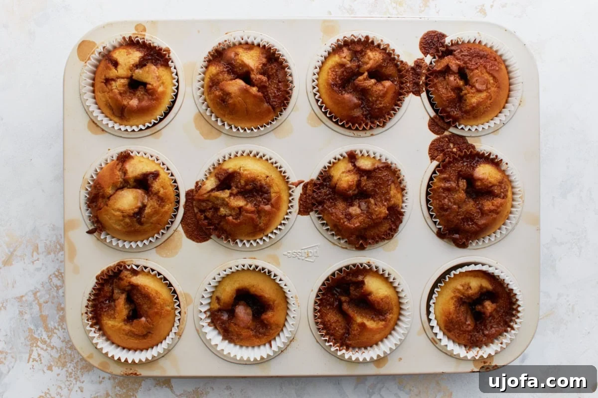 Gluten-Free Cinnamon Swirl Delights 11 Freshly baked gluten-free cinnamon roll muffins still in the tin, showing golden brown tops with caramelized cinnamon swirls.
