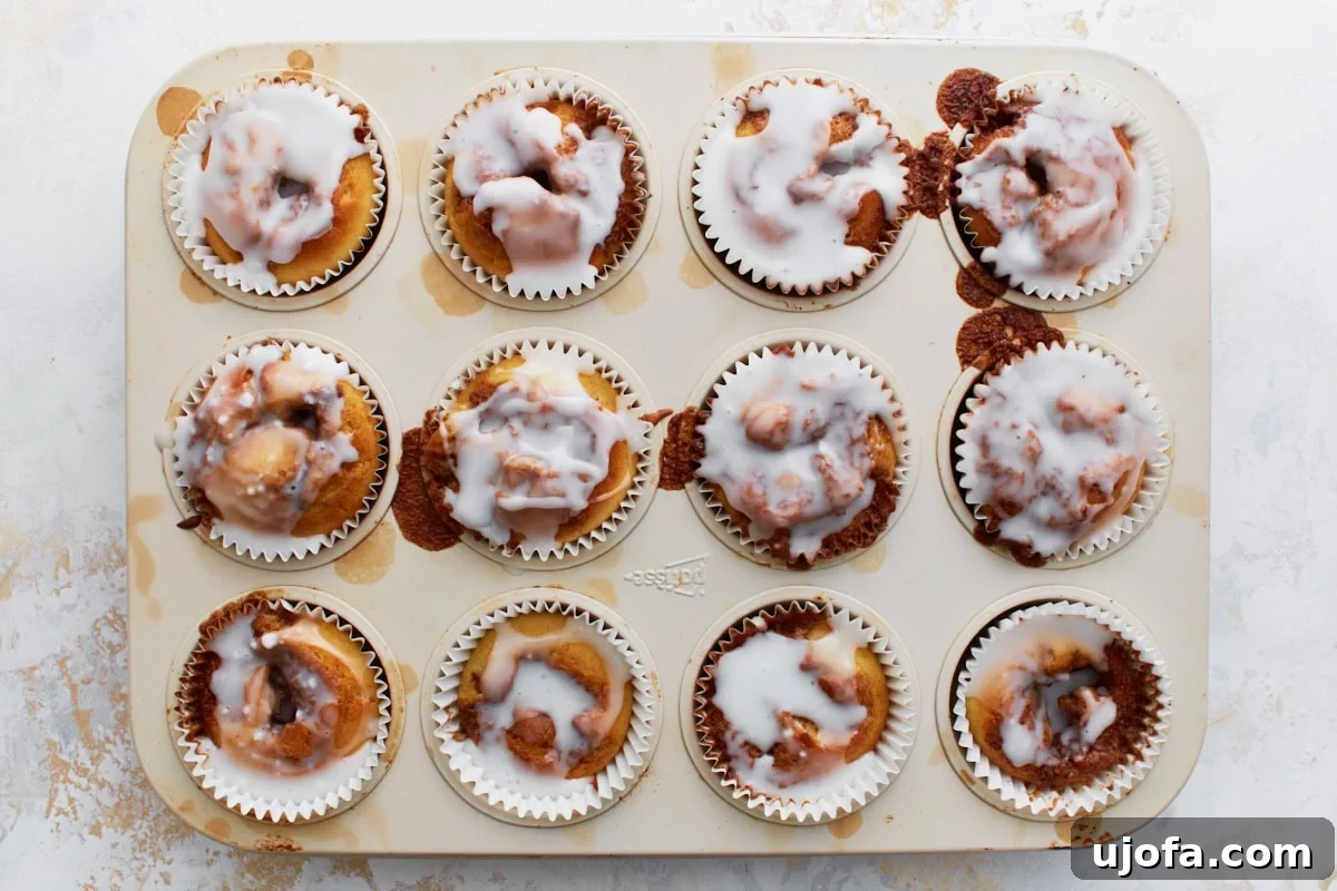 Gluten-Free Cinnamon Swirl Delights 13 Overhead view of a muffin tin filled with freshly baked gluten-free cinnamon roll muffins, each topped with a generous drizzle of vanilla glaze.