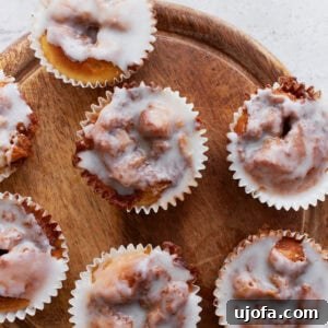 Overhead view of glazed gluten-free cinnamon roll muffins arranged on a round wooden board, showing their gooey swirls and shiny icing.