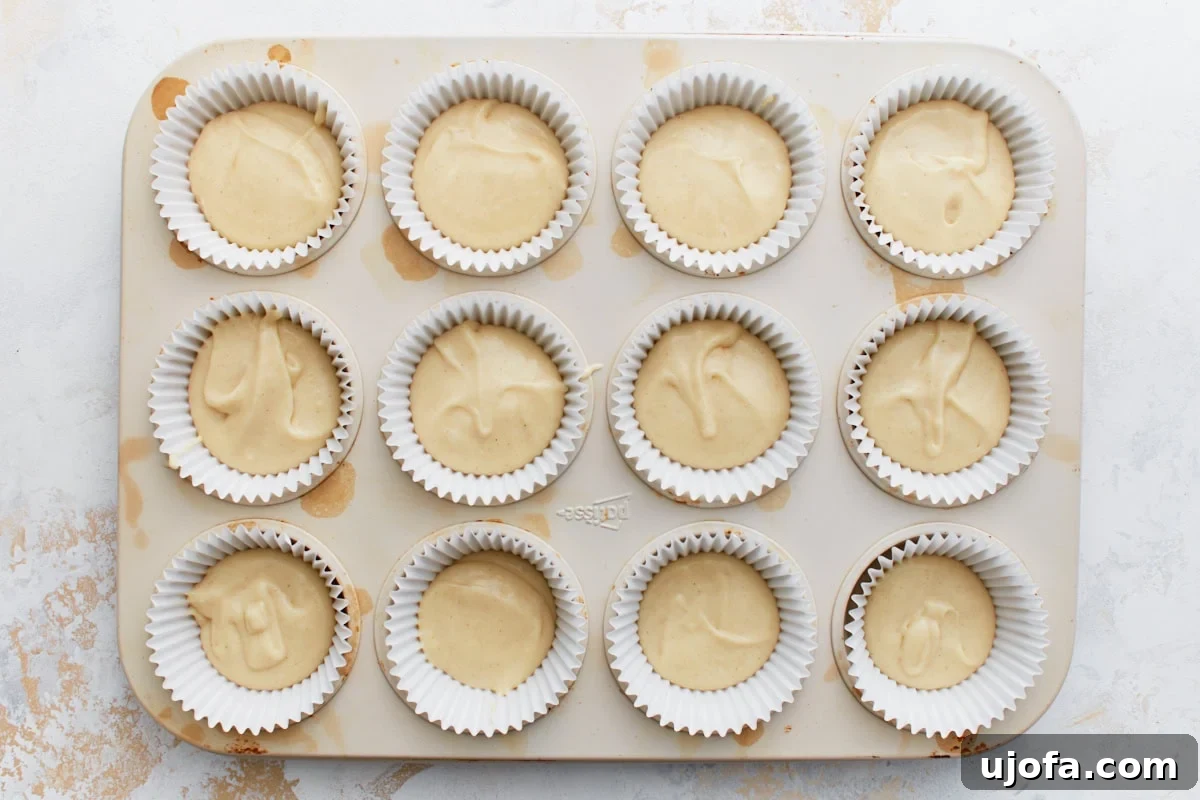 Gluten-Free Cinnamon Swirl Delights 7 Muffin tin lined with white paper liners, each filled with thick gluten-free batter, ready for the cinnamon topping.