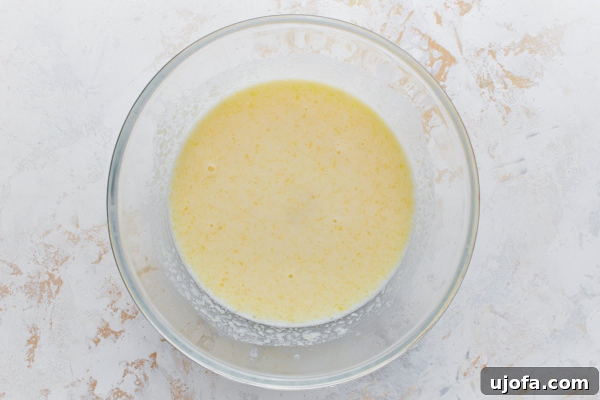 Hearty Buckwheat Flapjacks 6 A glass bowl containing a whisked wet ingredient mixture with a yellow hue, likely including eggs, milk, and melted butter, for making buckwheat pancakes.