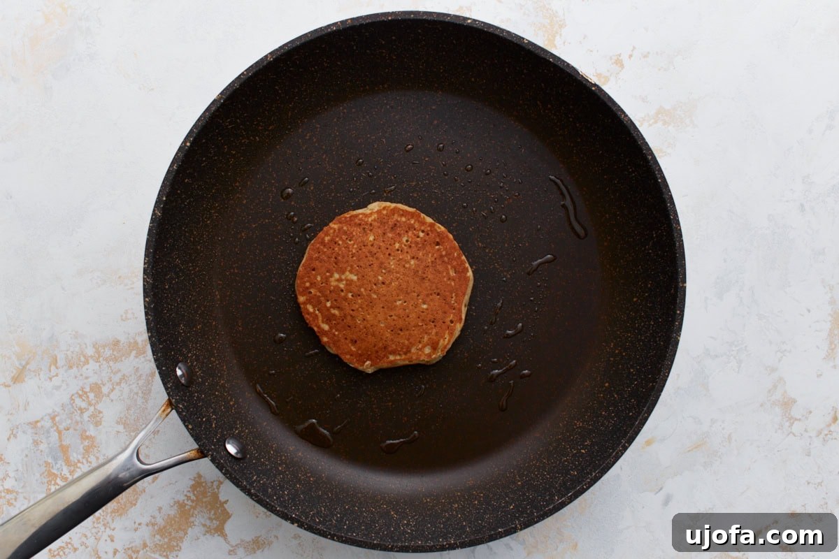Hearty Buckwheat Flapjacks 9 A fully cooked buckwheat pancake flipped to its golden-brown side, sitting in a non-stick pan with a bit of oil residue, ready to be plated.