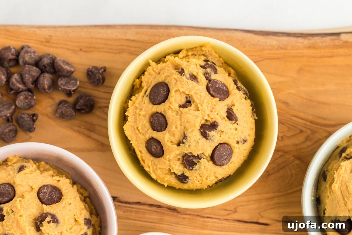 A close-up shot of a small yellow bowl filled with chickpea cookie dough, with chocolate chips embedded on top. Chocolate chips are scattered in the background.