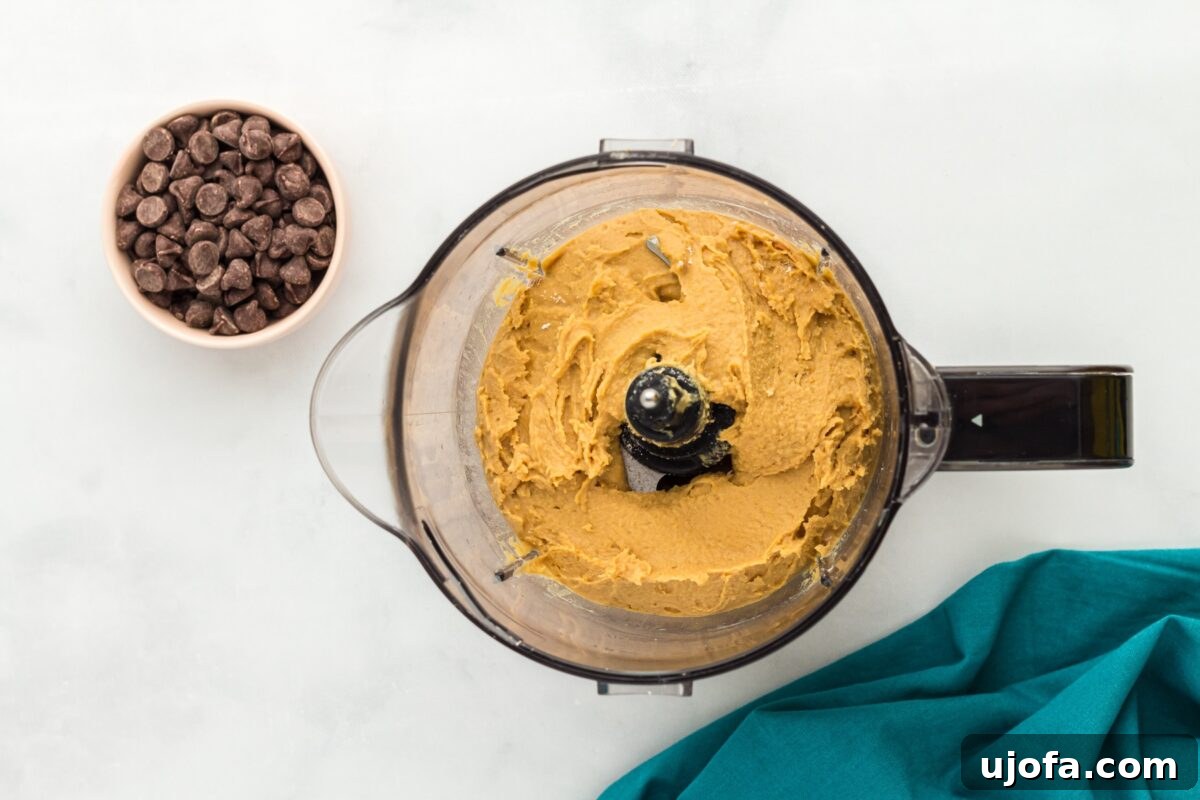 A food processor filled with blended chickpea cookie dough, showing a smooth and creamy texture.
