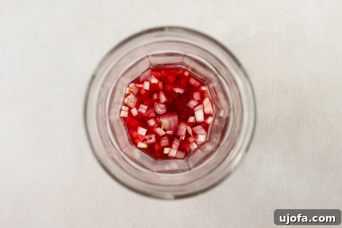 A close-up overhead shot of a glass jar filled with finely diced red onions soaking in a red liquid, likely vinegar, for pickling