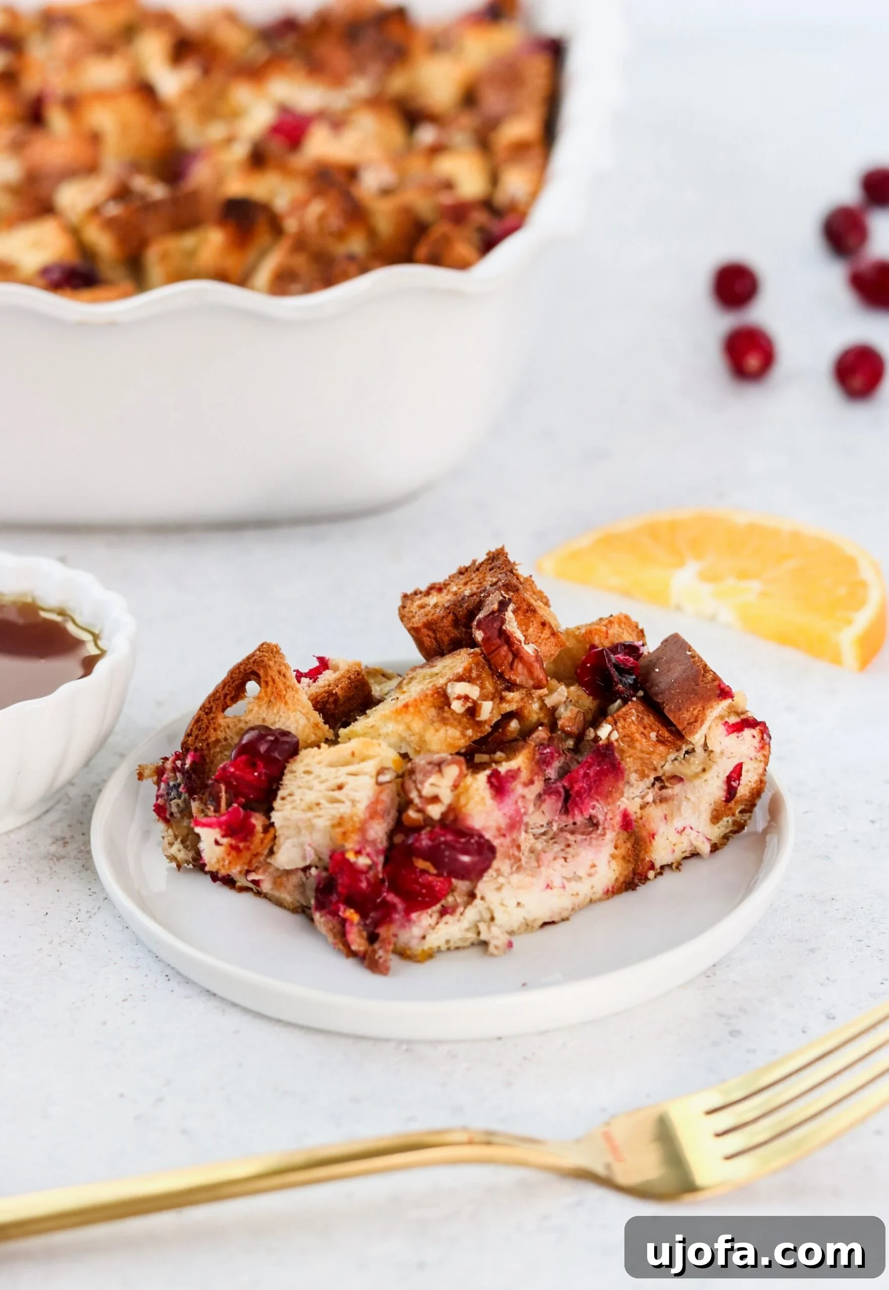 Close-up of French toast casserole batter soaking into bread chunks in a baking dish, with cranberries visible before chilling overnight.