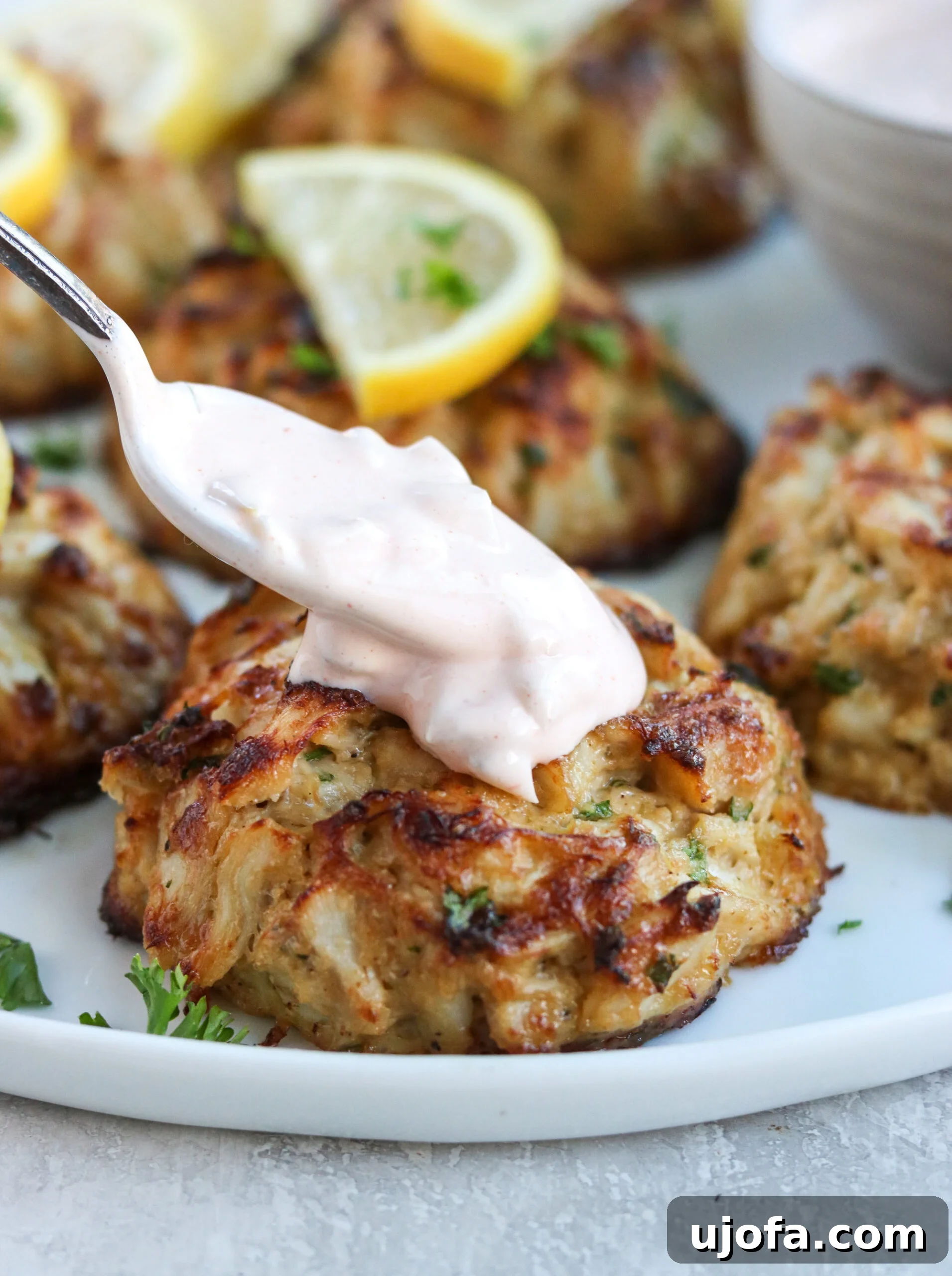 A hand gently topping a crispy crab cake with a dollop of zesty cocktail sauce, enhancing its flavor.