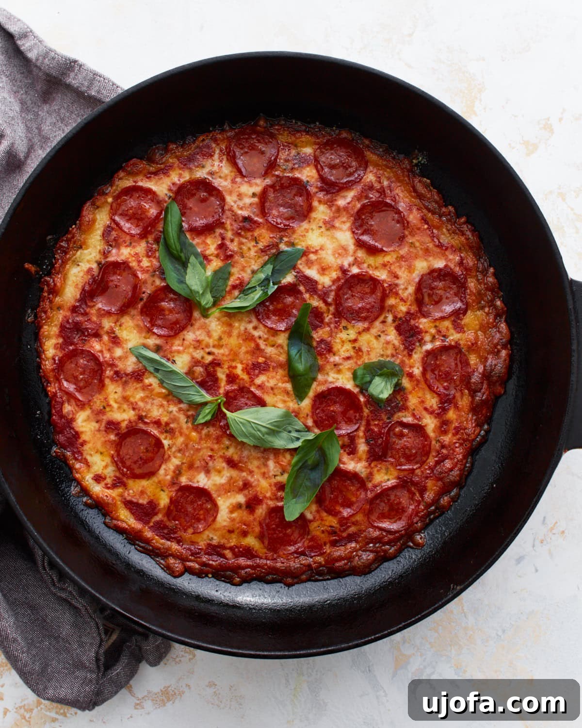 Pizza Bowl 2 Close-up of a fully baked crustless pepperoni pizza in a cast iron skillet, topped with fresh basil leaves. The melted cheese forms a golden-brown base, while vibrant red pepperoni and green basil provide a striking contrast.