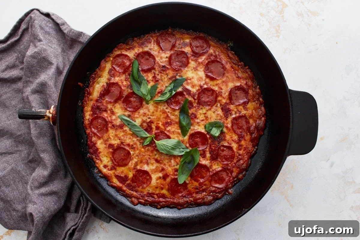 Pizza Bowl 10 Finished crustless pepperoni pizza in a cast iron skillet, beautifully garnished with fresh green basil leaves, ready to be served.