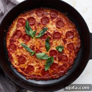 Close-up of a fully baked crustless pepperoni pizza in a cast iron skillet, topped with fresh basil leaves.
