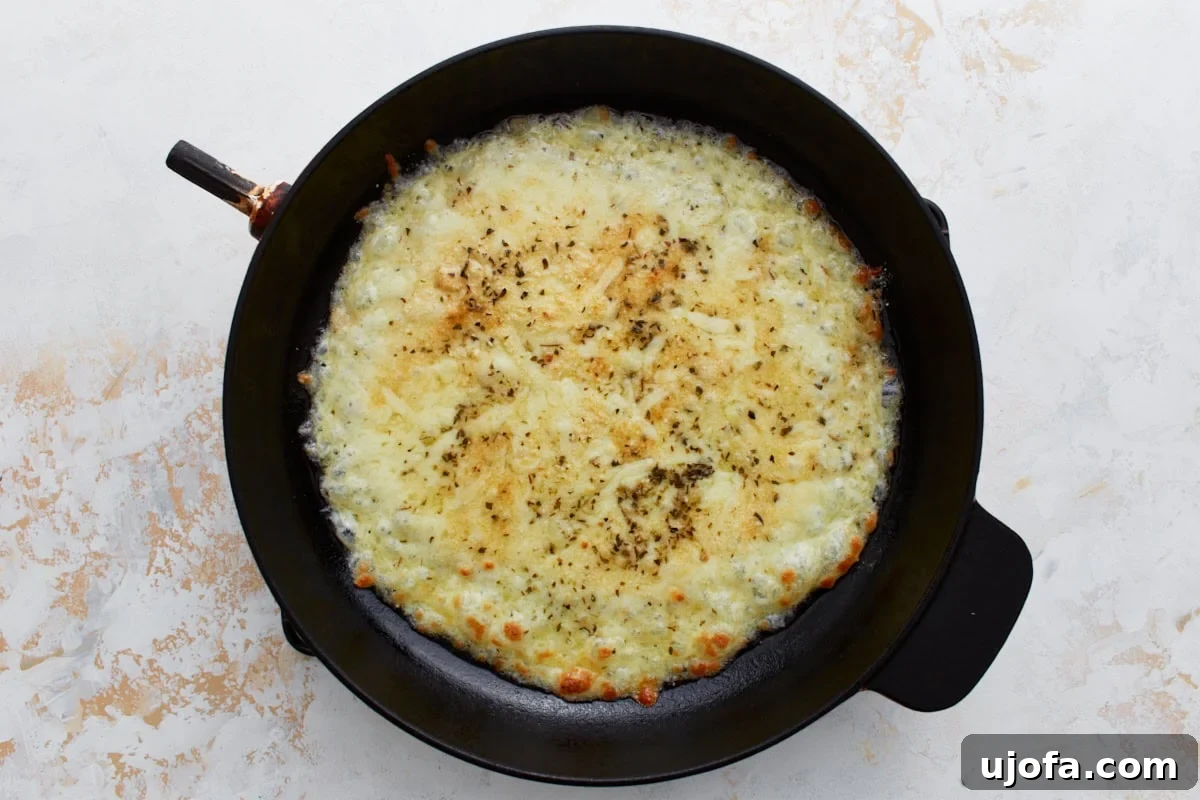Pizza Bowl 7 Melted cheese layer bubbling gently in the skillet after its initial bake, showing golden edges and ready for toppings.