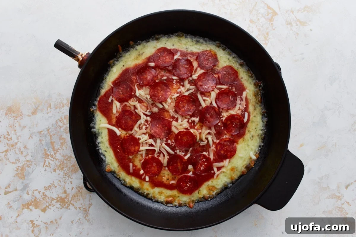 Pizza Bowl 8 Pizza sauce, vibrant red pepperoni, and an additional sprinkle of cheese layered on top of the already melted cheese base in the skillet.