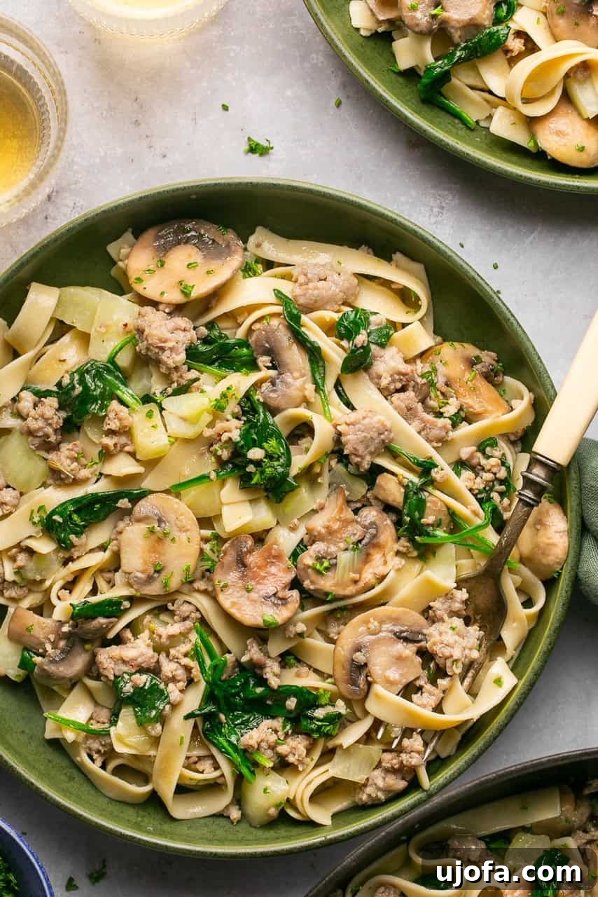 sausage and fennel pasta with spinach and mushrooms in a bowl with a fork, ready to be enjoyed