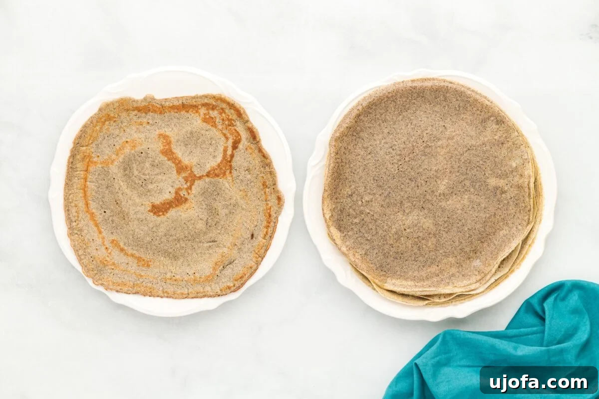 Savory Buckwheat Galettes 10 Two white plates displayed side by side: one holds a neat stack of uniformly cooked buckwheat crepes, while the other features a single crepe with distinctly darker, more pronounced browned spots, illustrating variations in cooking.