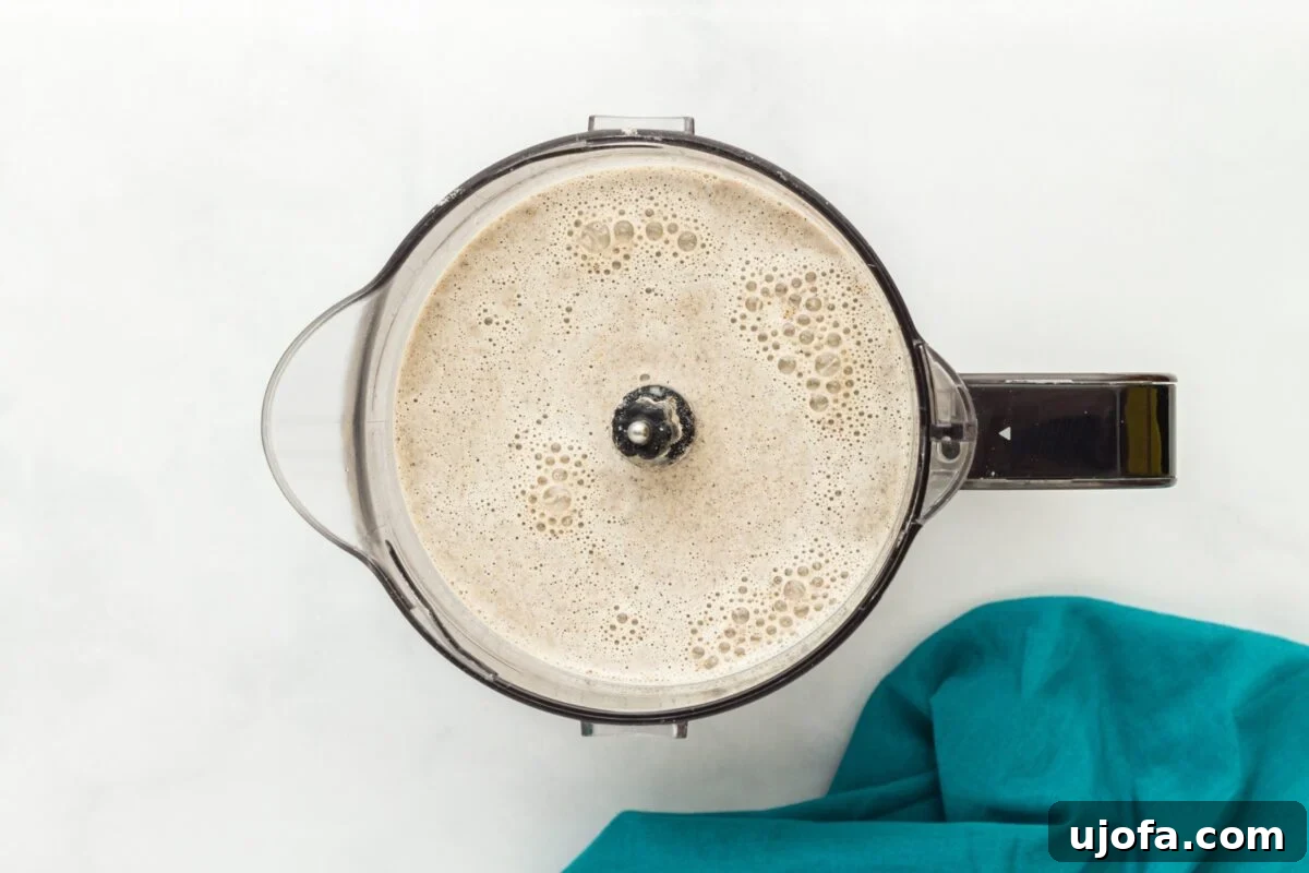 Savory Buckwheat Galettes 5 A blender filled with a frothy, smooth buckwheat crepe batter, positioned on a clean white surface alongside a decorative teal napkin, indicating readiness for cooking.