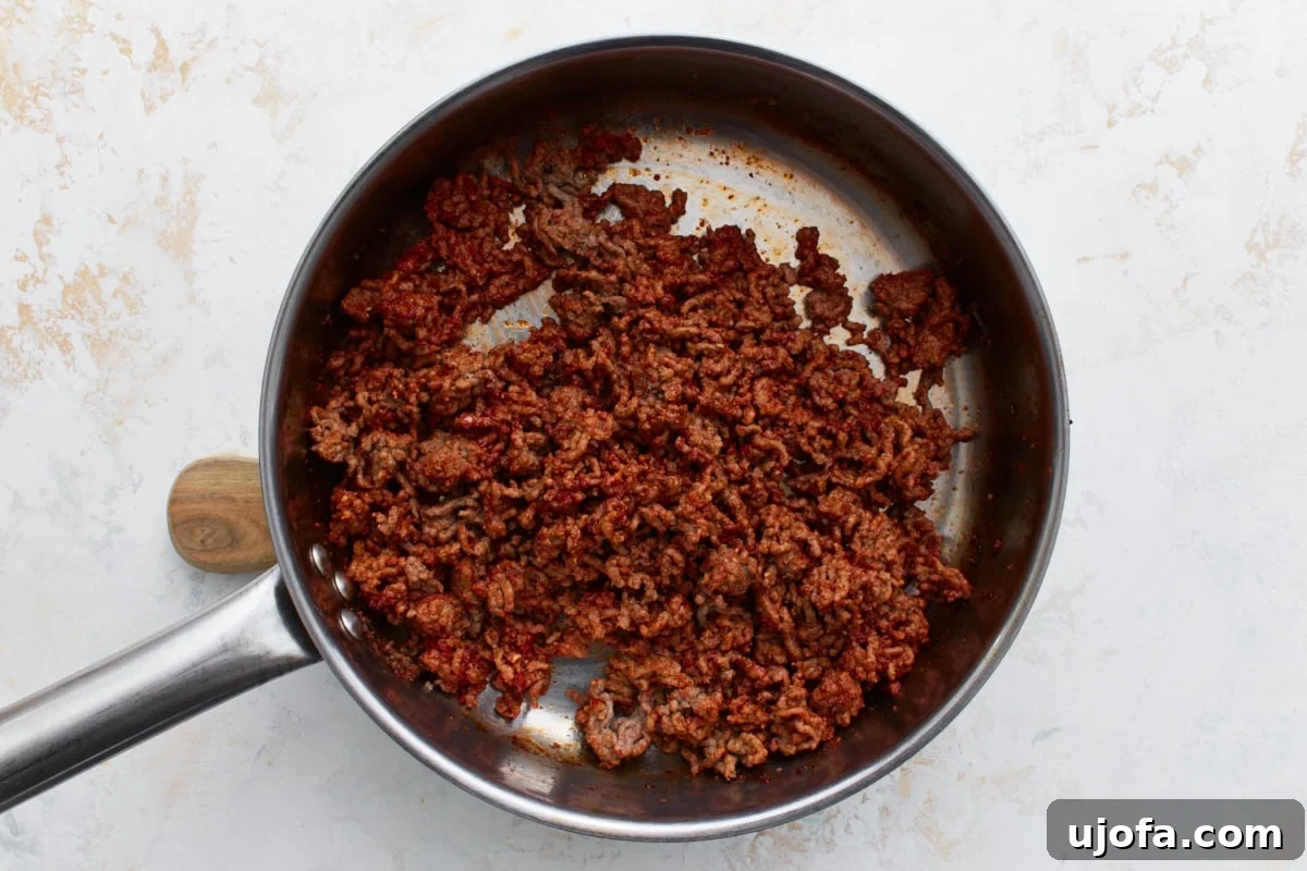 Cooked ground beef coated evenly in a vibrant red tomato paste and a blend of spices, mixed well in a skillet on a light background, enhancing its rich color.