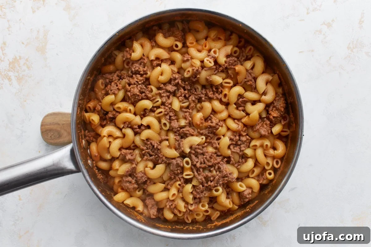 Gluten-free pasta and beef mixture in the skillet, with most of the liquid absorbed and the sauce visibly thickening as the pasta cooks to perfection.