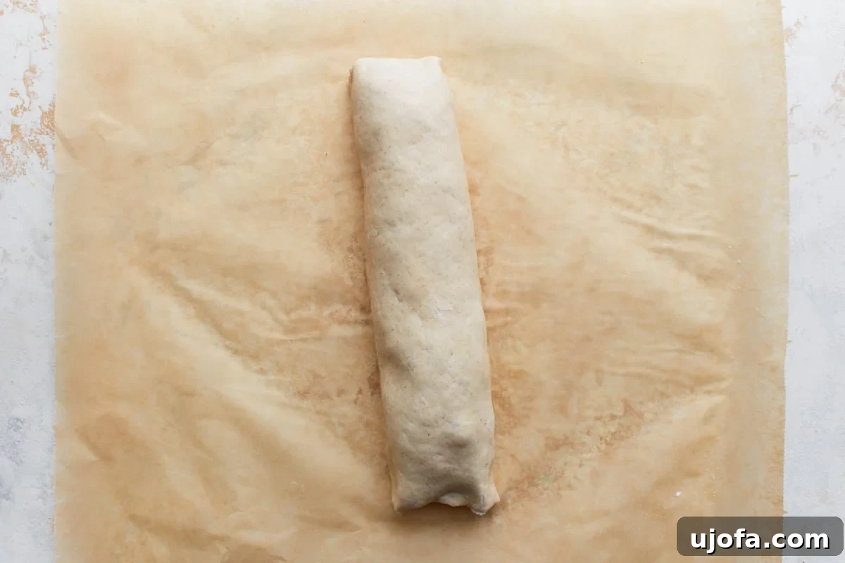 Rolled-up log of gluten-free pizza dough filled with cheese and pepperoni, placed neatly seam-side down on parchment paper, ready for slicing.