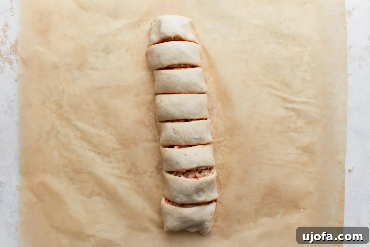 Rolled gluten-free pizza dough log perfectly sliced into eight individual, even pieces, forming distinct pizza rolls before baking.