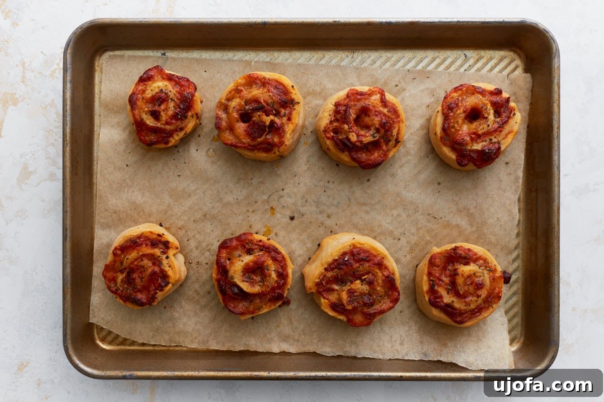 A baking sheet filled with perfectly golden-brown, freshly baked gluten-free pizza rolls, with melted cheese oozing slightly from the edges.