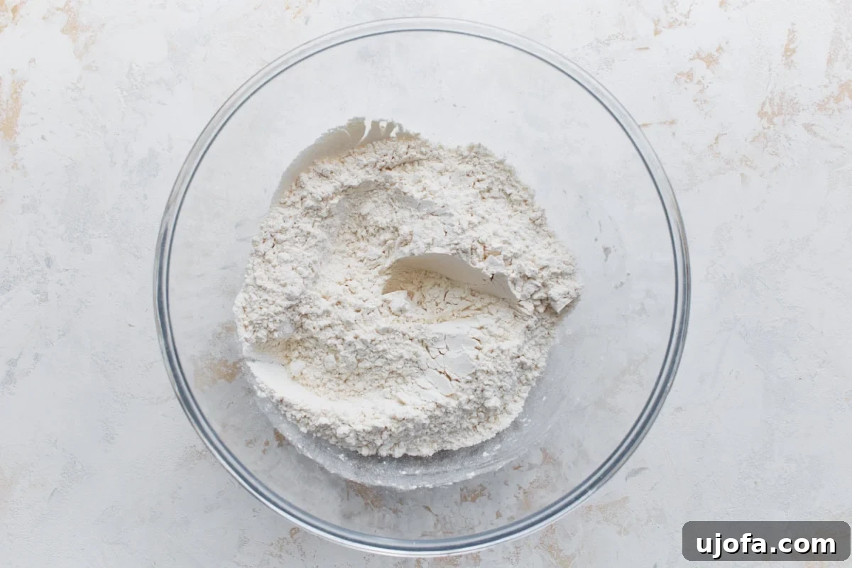 Overhead view of gluten-free flour mixture in a clear mixing bowl on a light surface, showing flour, xanthan gum, baking powder, and salt combined.
