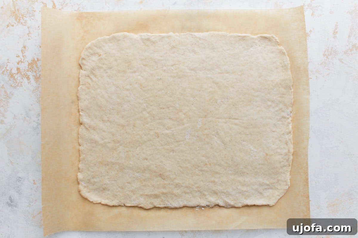 Flattened gluten-free dough rolled into a large, even rectangle on parchment paper, providing a perfect base for the pizza roll toppings.