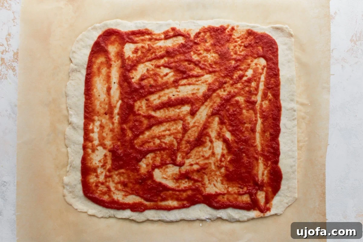 Rectangular gluten-free dough topped with an even layer of vibrant red pizza sauce, deliberately leaving a clean border around all the edges.