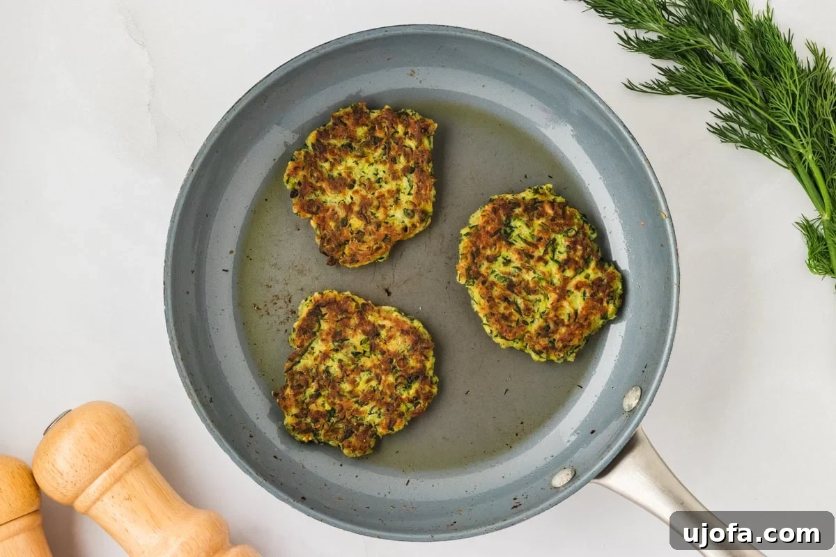 Three golden-brown zucchini fritters flipped to their cooked side in the skillet, showing crisp, even browning.