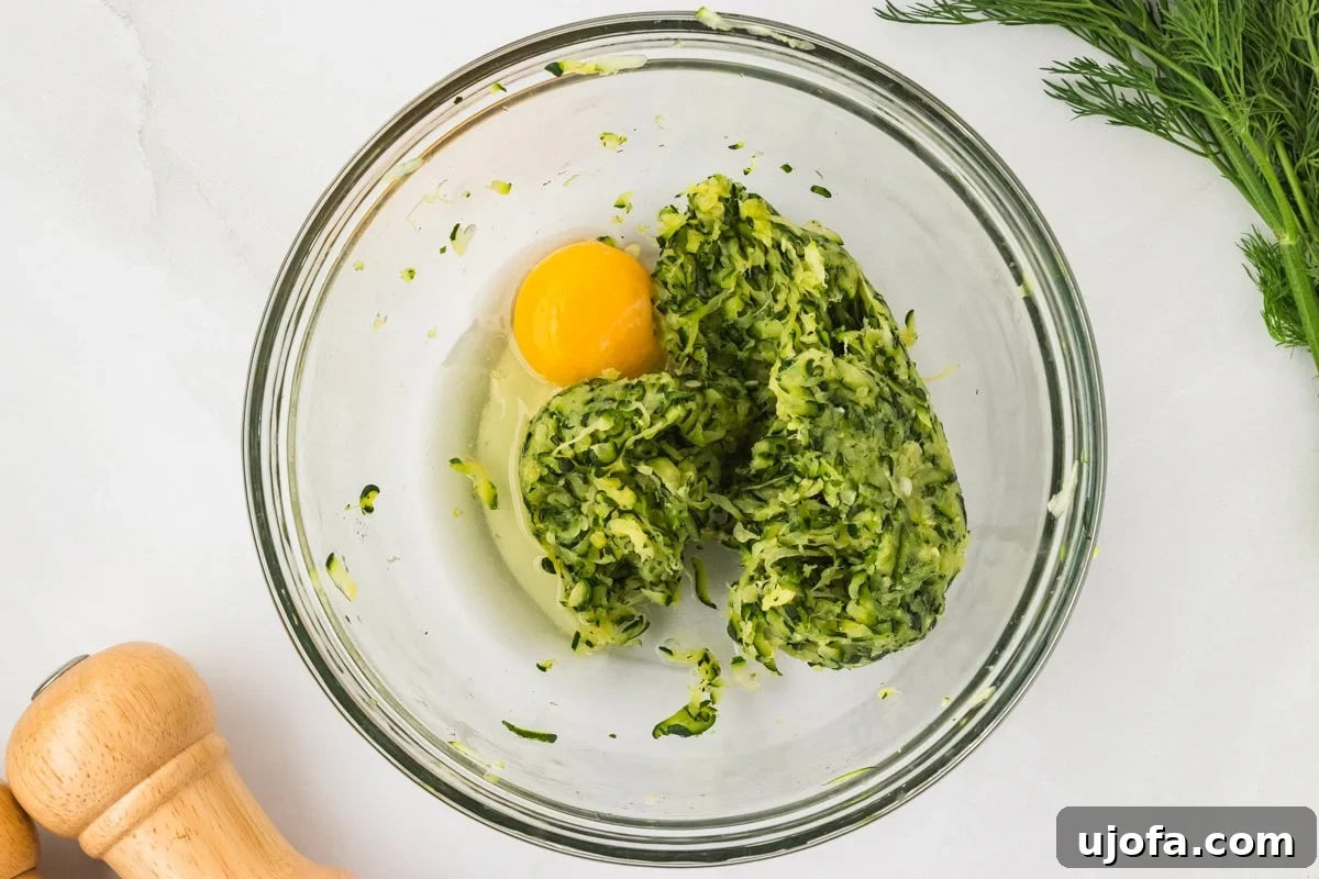 A cracked raw egg added to the bowl of drained zucchini, ready to be mixed in for the batter.
