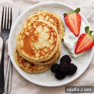 A stack of golden gluten-free protein pancakes on a white plate, served with blackberries, halved strawberries, and a dollop of Greek yogurt.