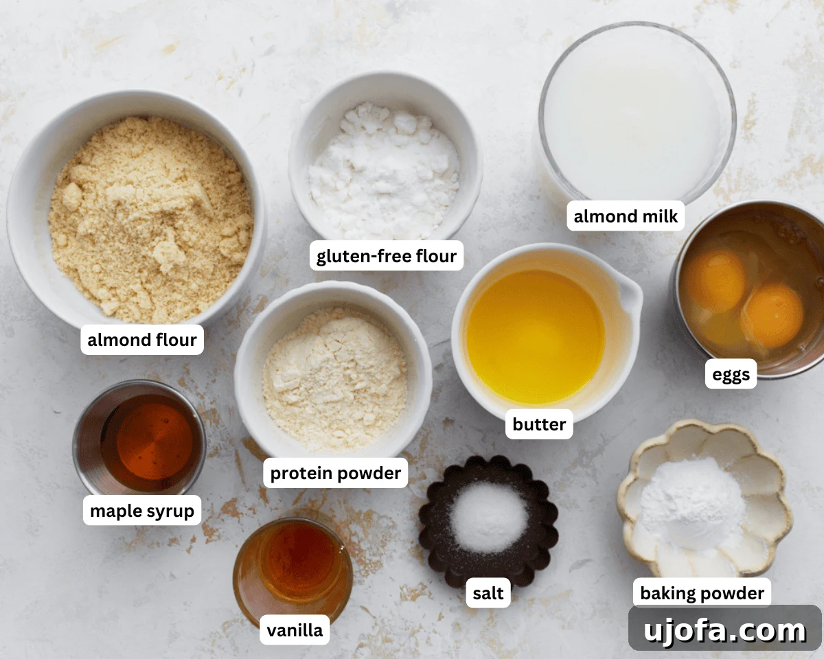 A collection of ingredients for gluten-free protein pancakes, including almond flour, gluten-free flour, protein powder, eggs, milk, and butter, neatly laid out on a kitchen counter.
