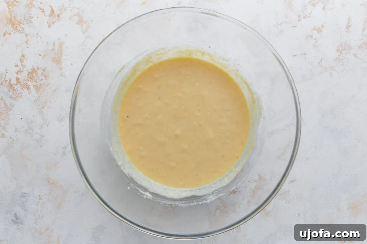 A glass bowl of fully mixed pancake batter, smooth and slightly thick with small bubbles forming, indicating it's ready to rest.