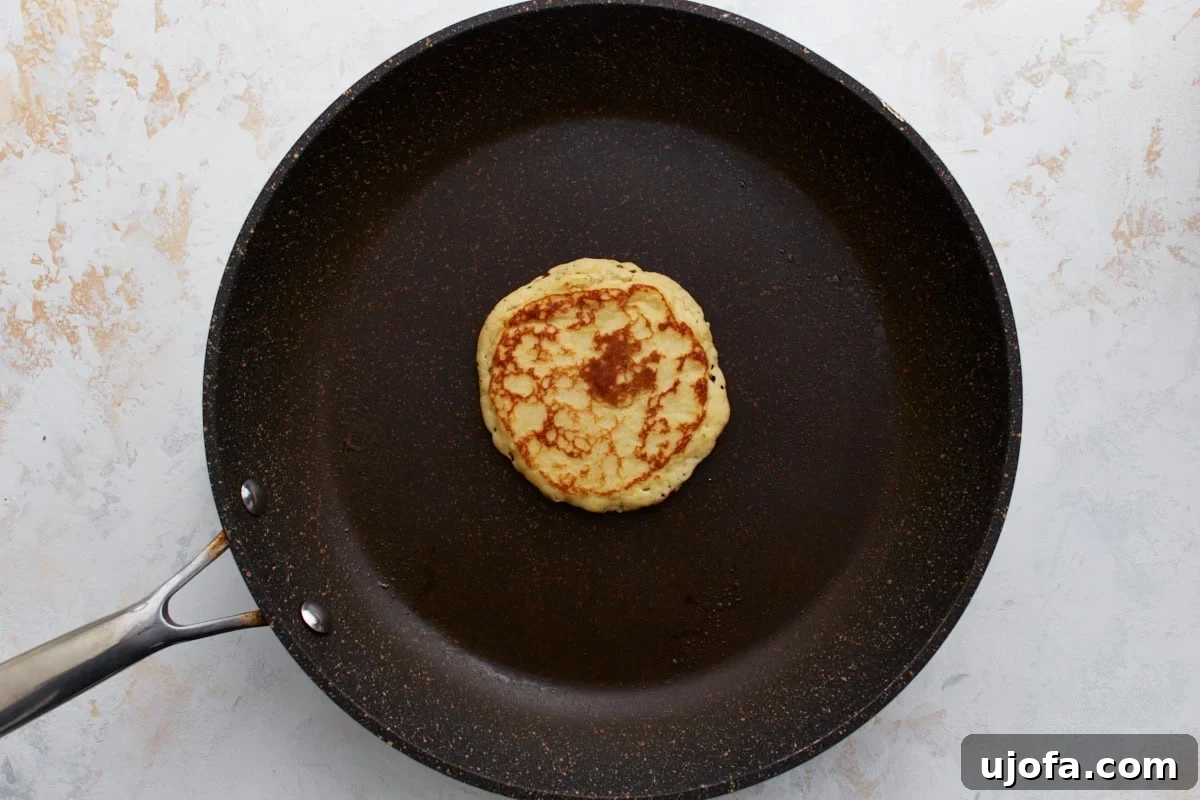 A perfectly golden-brown pancake, just flipped, cooking on its second side in a non-stick skillet, creating a delicious aroma.