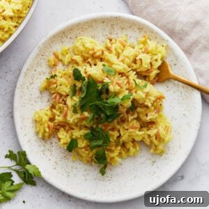 A serving of golden gluten-free rice pilaf garnished with chopped parsley on a speckled white plate with a gold fork.