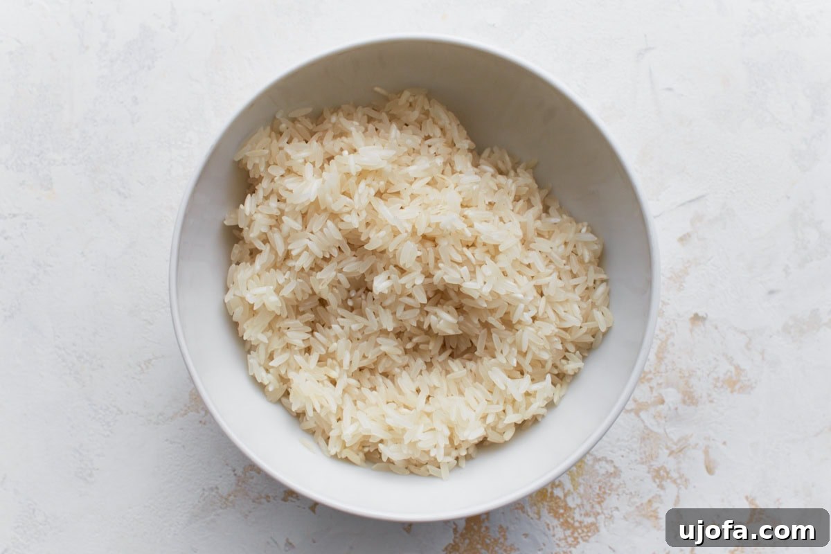 A white bowl filled with thoroughly rinsed, uncooked long-grain white rice, ready for cooking.