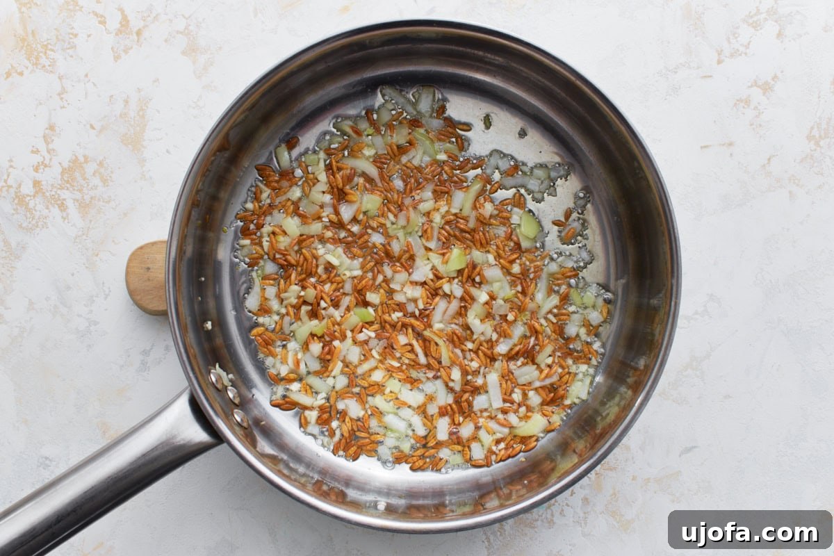 Diced onions added to the toasted gluten-free orzo in a pan, beginning to soften and turn translucent as they sauté.