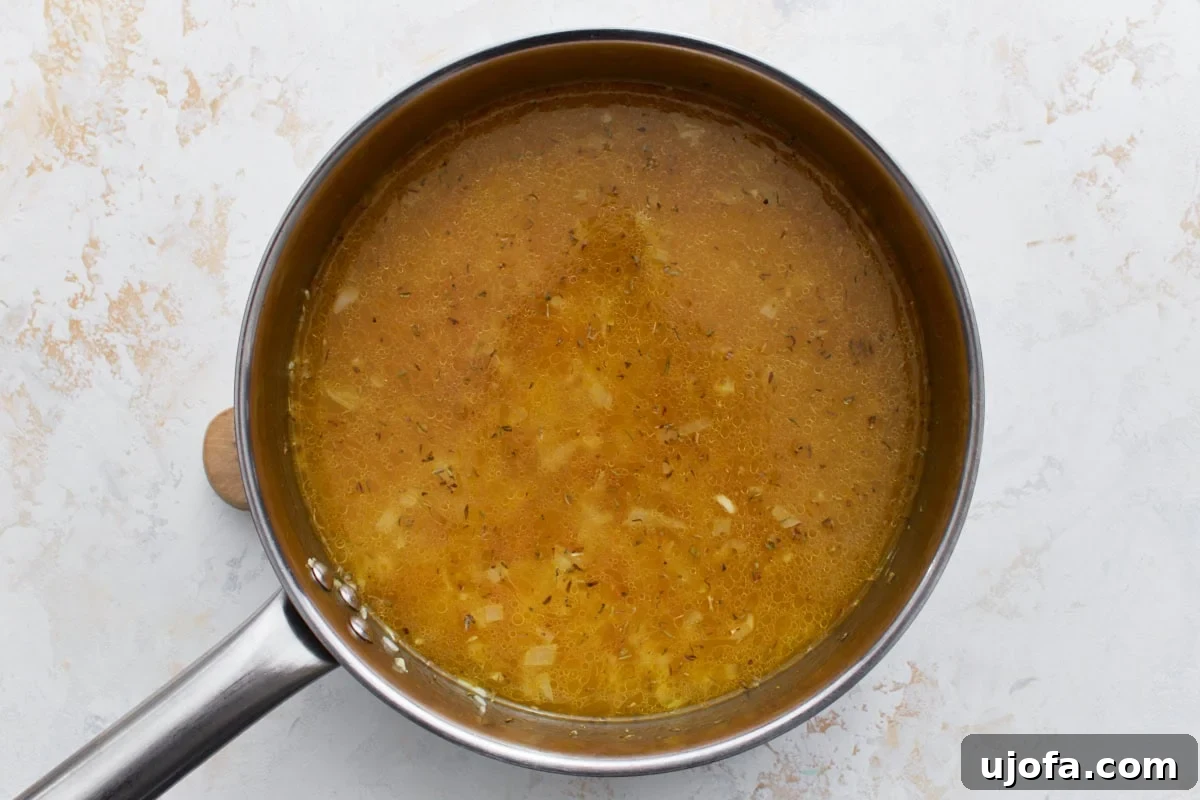 Chicken broth and a blend of seasonings added to the pan with rice and pasta, beginning to simmer and infuse with flavor.