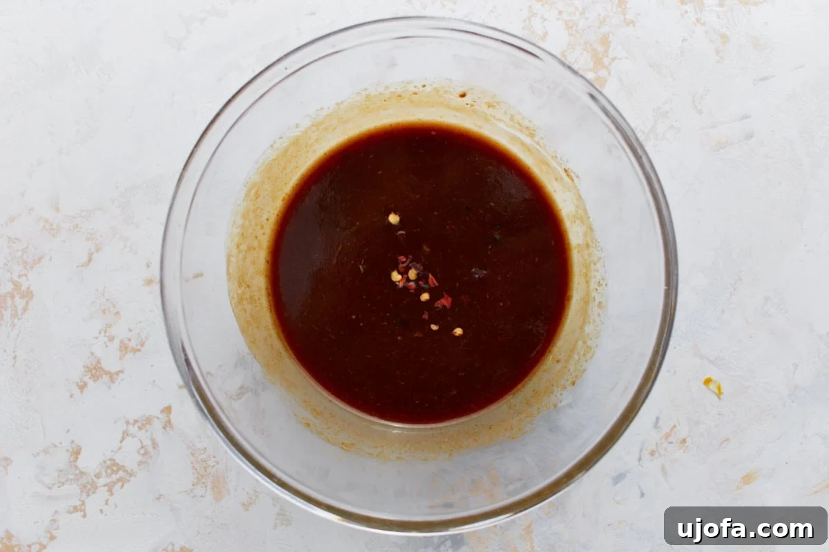 Glass bowl of homemade dipping sauce with chili flakes on top, set on a light stone background.