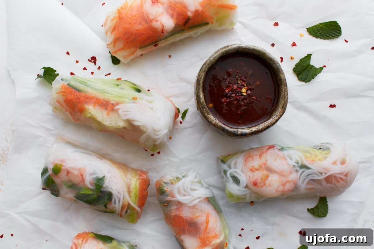 Platter of finished Vietnamese summer rolls arranged around a bowl of dipping sauce, garnished with fresh mint and red pepper flakes.