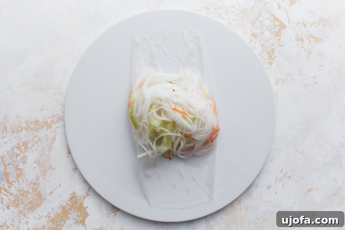 Rice paper wrapper filled with vermicelli noodles, shredded carrots, and cucumber placed in the center, ready to be rolled.
