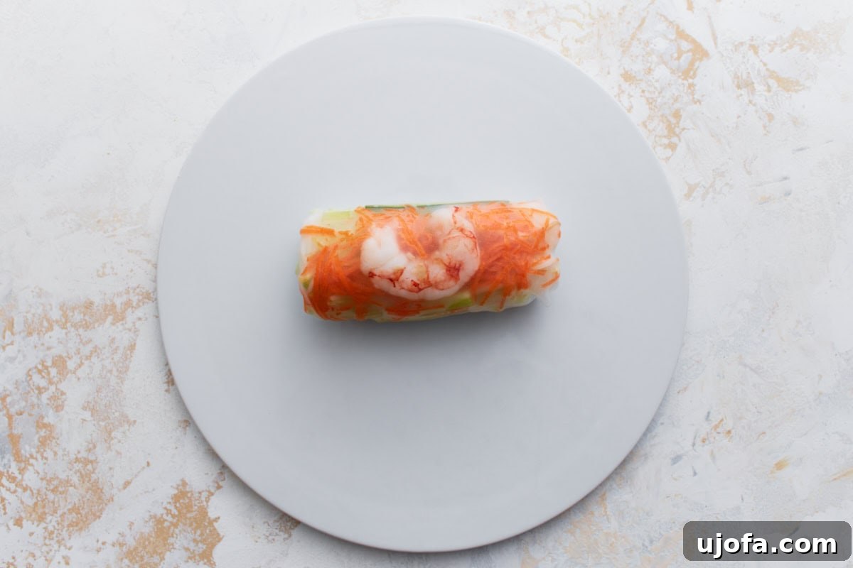 Fully rolled Vietnamese summer roll showcasing shrimp and shredded carrots through the translucent rice paper wrapper.